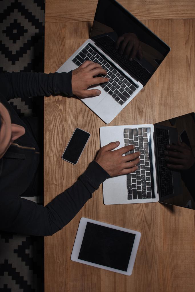 Masa üstü smartphone ve tablet, siber güvenlik kavramı ile dizüstü bilgisayarlar kullanarak siyah hoodie hacker havai görünümü - Fotoğraf, Görsel