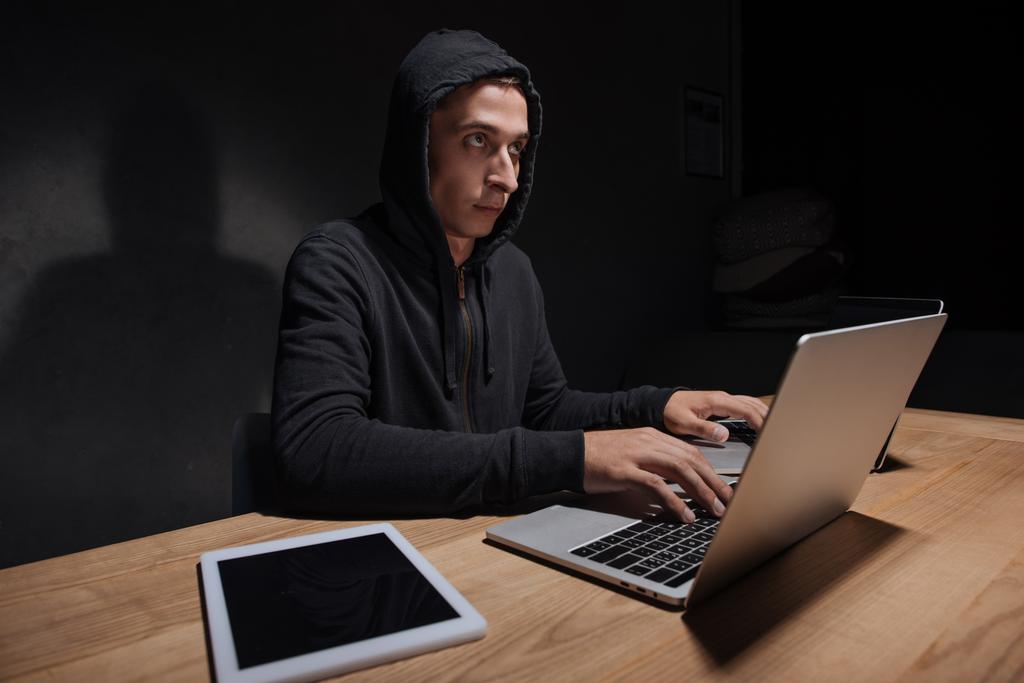 Csákányos-ban használ laptop a sötét szobában, számítógépes biztonsági koncepció tabletta asztali fekete kapucnis - Fotó, kép