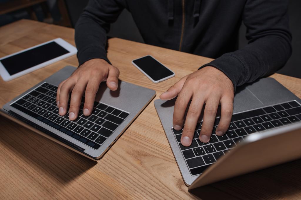 visão parcial do hacker usando laptops em mesa com smartphone e tablet, conceito de segurança cibernética
 - Foto, Imagem