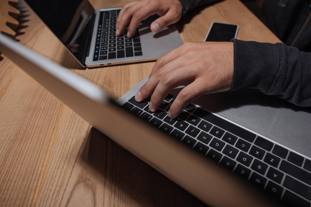 частковий вид хакера з використанням ноутбуків на стільниці зі смартфоном, концепція кібербезпеки
 - Фото, зображення