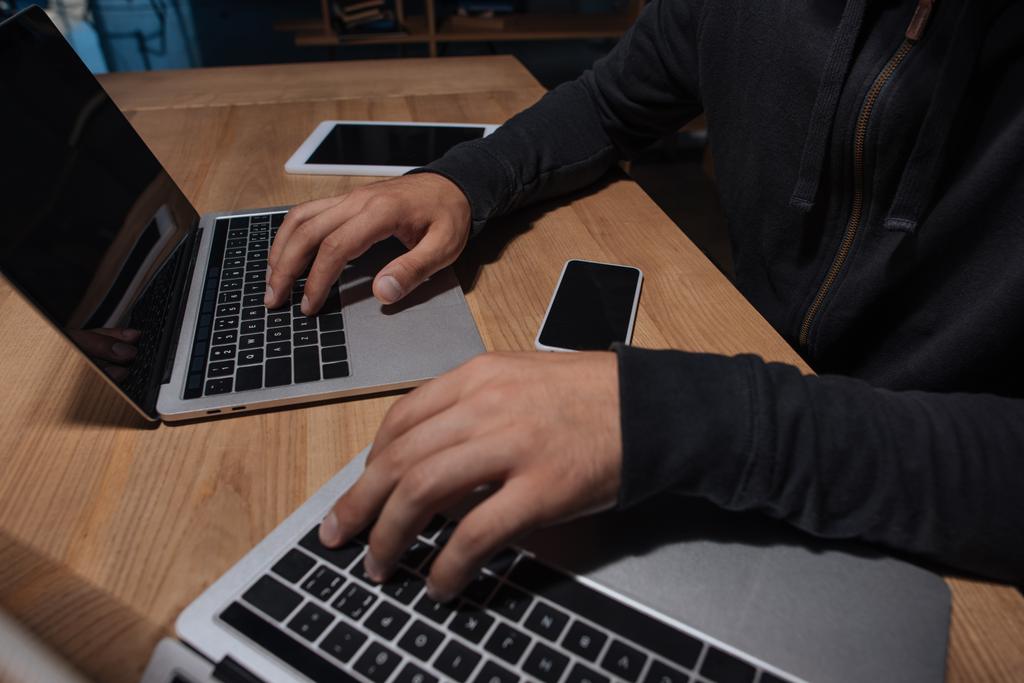 Μερική άποψη των αρσενικών χάκερ χρησιμοποιούν φορητούς υπολογιστές στο tabletop με smartphone και tablet, έννοια της ασφάλειας στον κυβερνοχώρο - Φωτογραφία, εικόνα
