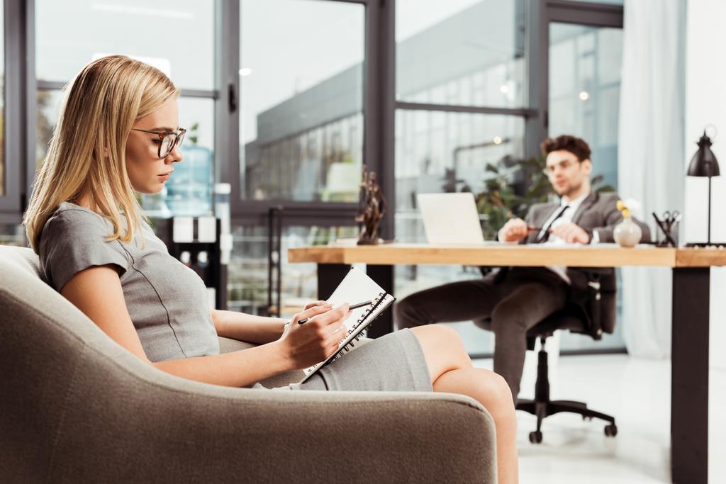donna d'affari che prende appunti nel quaderno mentre siede in poltrona con un collega sul posto di lavoro in ufficio
 - Foto, immagini