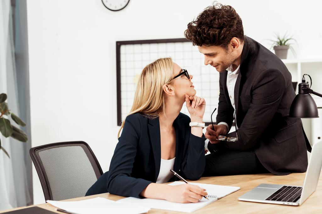 Zijaanzicht van jonge ondernemers kijken elkaar op werkplek, flirten en office romance-concept - Foto, afbeelding