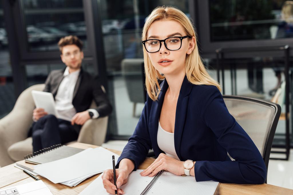 foco seletivo de empresário que olha para mulher de negócios em óculos que olha para câmera no local de trabalho no escritório
 - Foto, Imagem