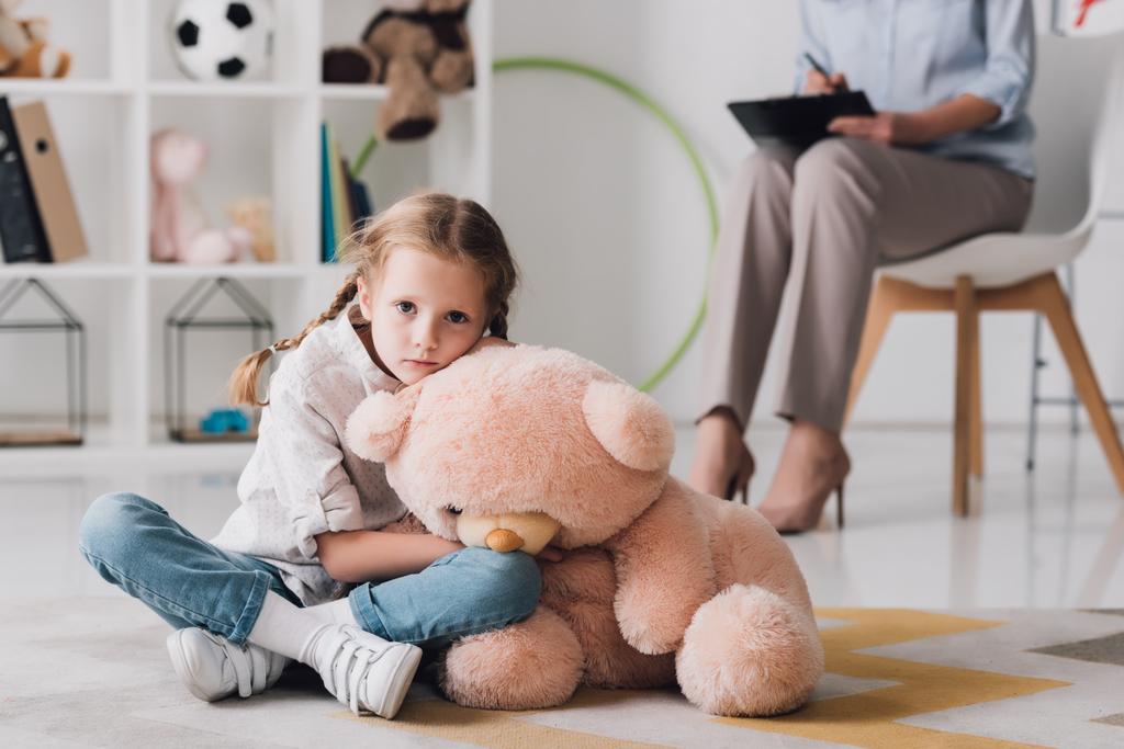 szomorú kisgyermek ült a padlón ülő-on háttér pszichológus teddy medve - Fotó, kép
