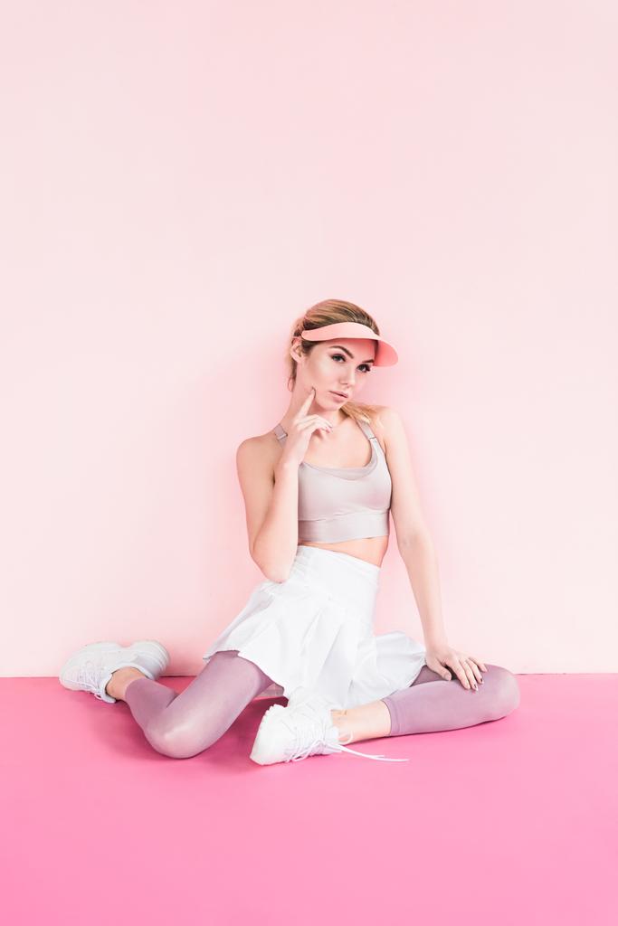 pensive stylish sportswoman in visor hat posing on pink - Photo, Image
