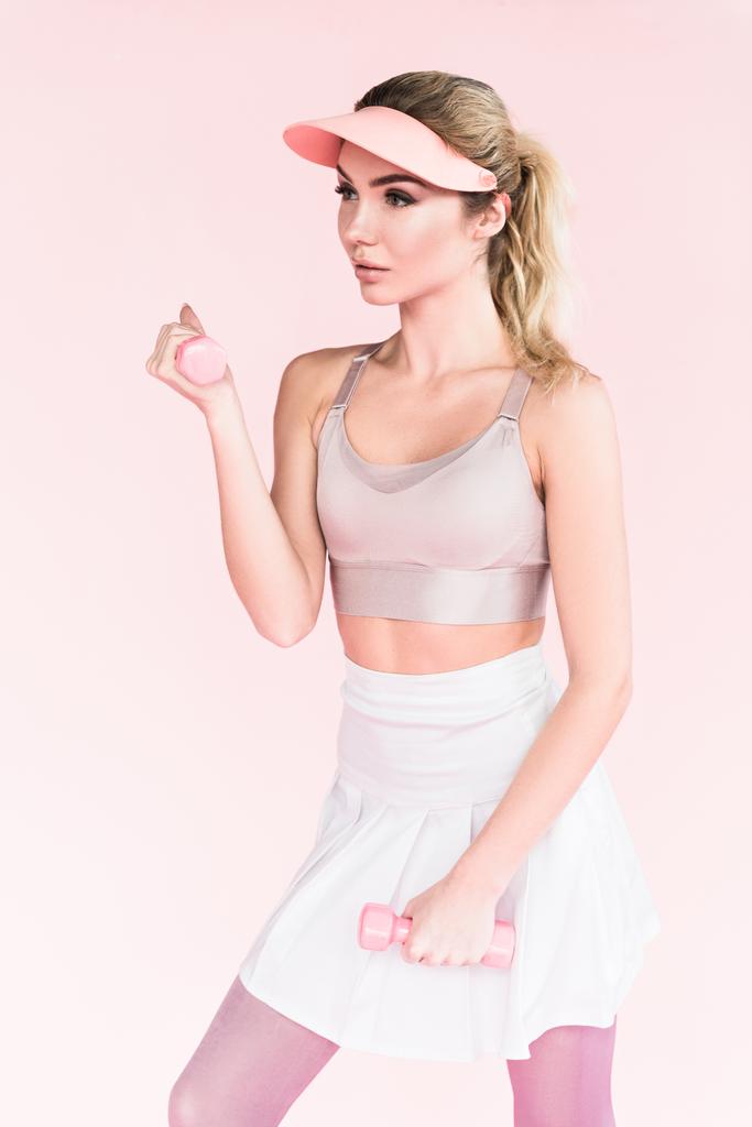 bonita atleta en sombrero de visera haciendo ejercicio con pesas en rosa
 - Foto, Imagen