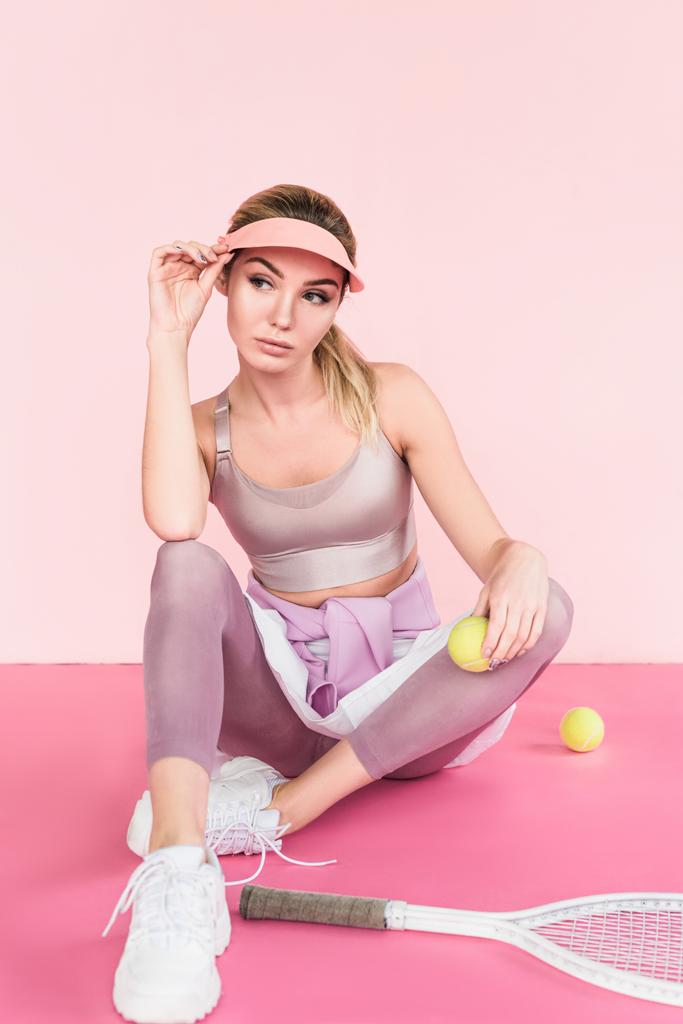 stylish sportswoman in visor hat posing with tennis racket and balls on pink - Photo, Image
