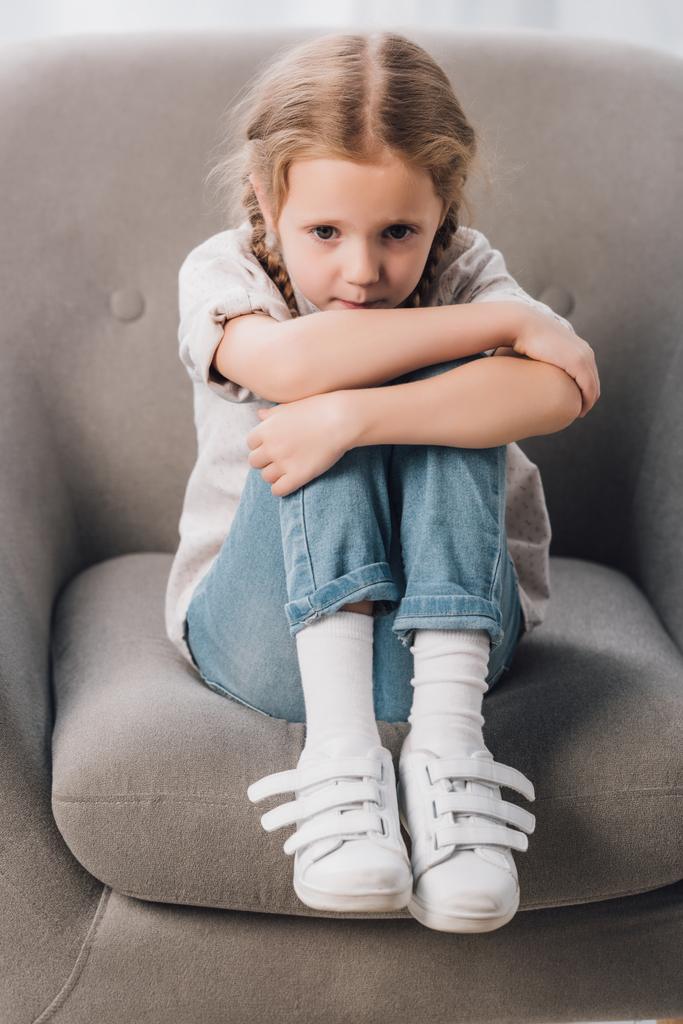 lonely little child sitting in armchair and looking at camera - Photo, Image