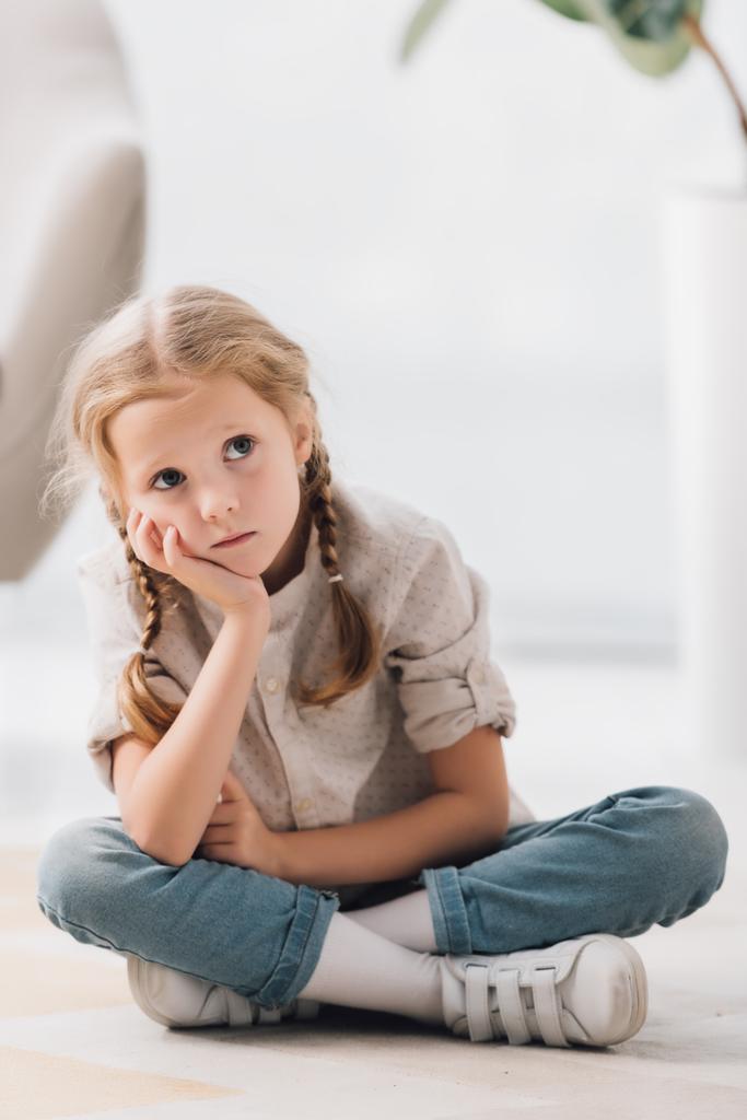 promyšlené malé dítě sedí na podlaze prázdné místnosti a vyhledávání - Fotografie, Obrázek