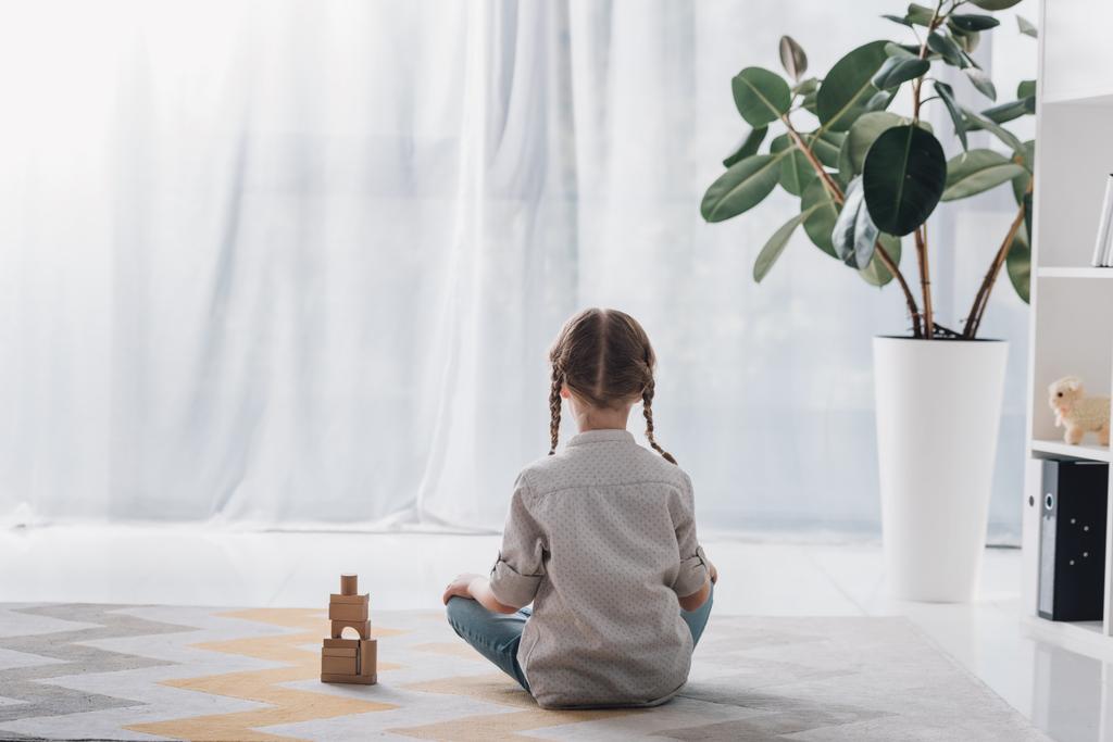 visão traseira da criança sentada no chão com blocos de madeira e olhando para longe
 - Foto, Imagem