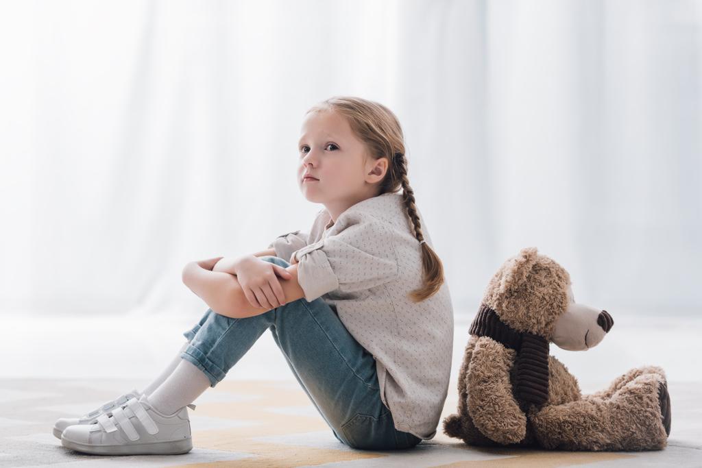 Μερική άποψη του κατάθλιψη μικρό παιδί που κάθονται στο πάτωμα πλάτη με πλάτη με αρκουδάκι - Φωτογραφία, εικόνα