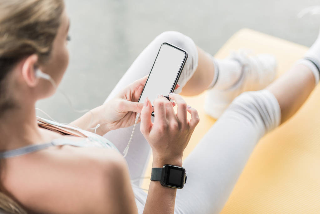 vista parcial de la deportista con smartwatch usando smartphone cerca de la pelota de fitness en el gimnasio
 - Foto, Imagen