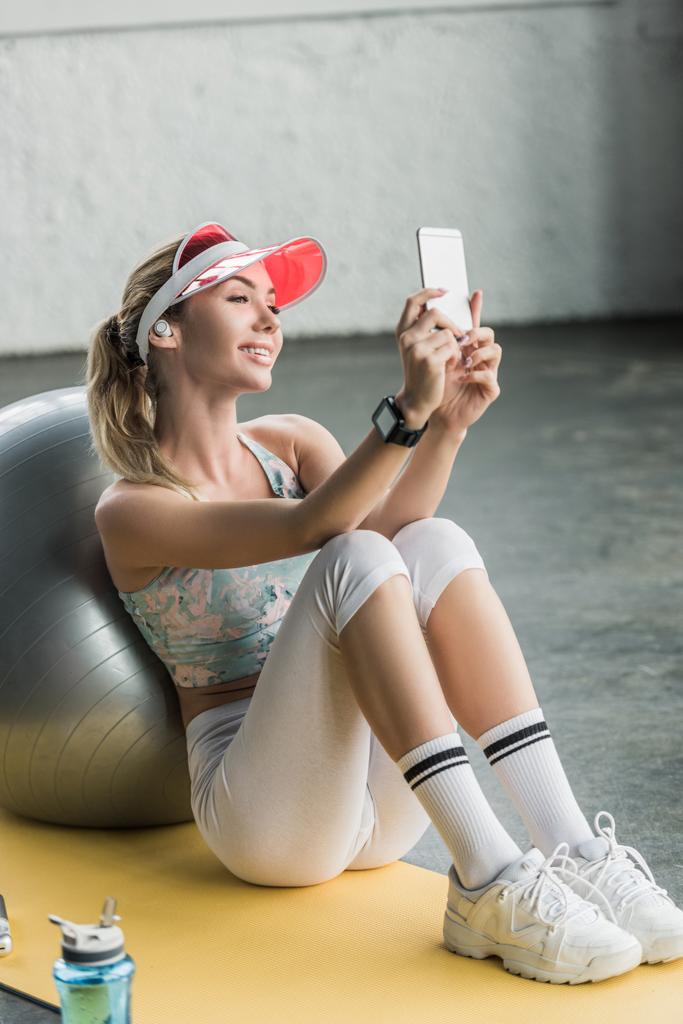 счастливая спортсменка со смартфоном, делающая селфи на смартфоне возле фитнес-мяча в тренажерном зале
 - Фото, изображение
