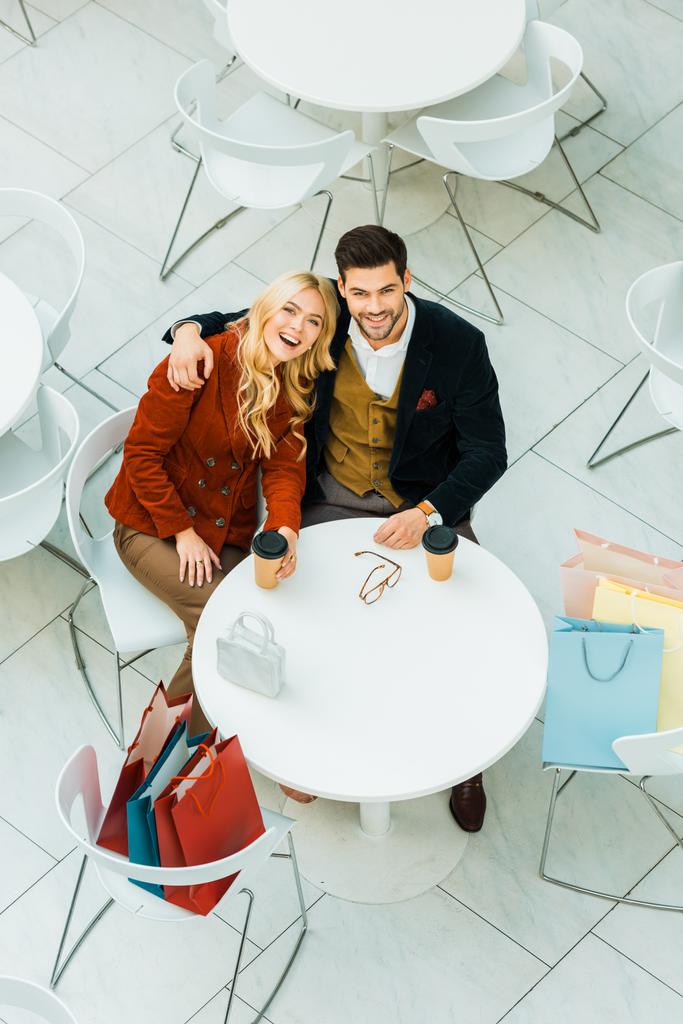 vista aerea della coppia felice con borse della spesa che si abbracciano e si siedono nel caffè
   - Foto, immagini