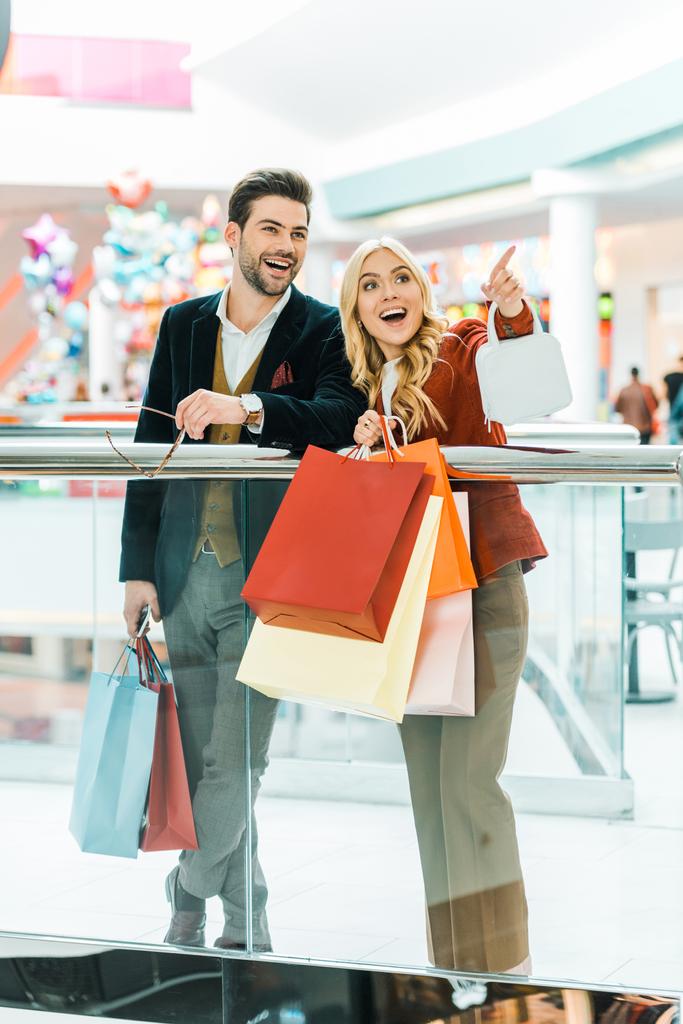 young couple with shopping bags spending time in shopping mall, woman showing something - Photo, Image