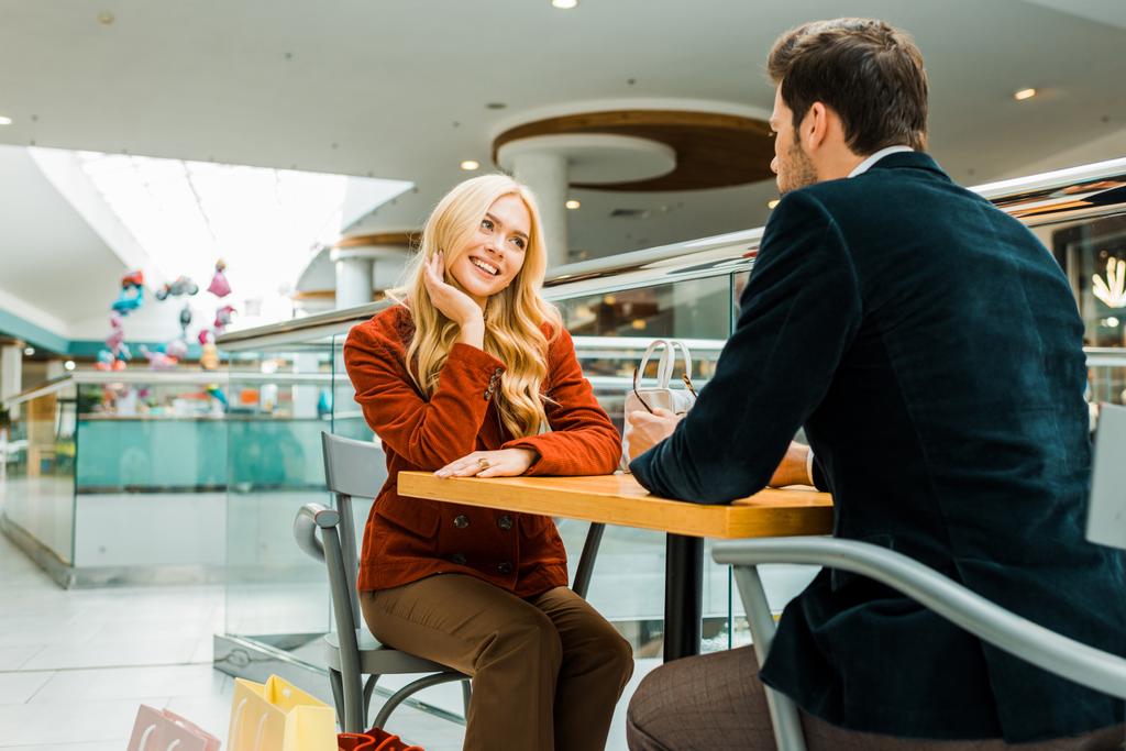 ευτυχισμένο ζευγάρι βλέπουν ο ένας τον άλλον και να κάθεται με τσάντες αγορών σε καφετέρια στο εμπορικό κέντρο - Φωτογραφία, εικόνα