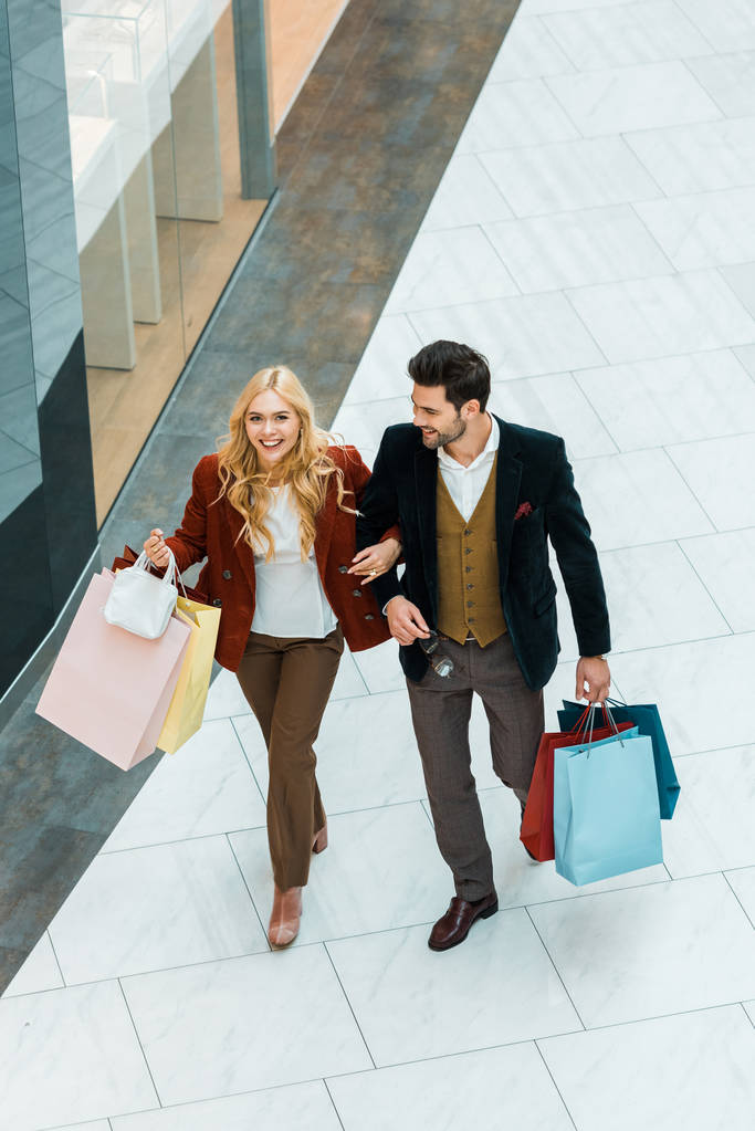 vista aérea de pareja feliz con bolsas de compras caminando en el centro comercial
 - Foto, imagen
