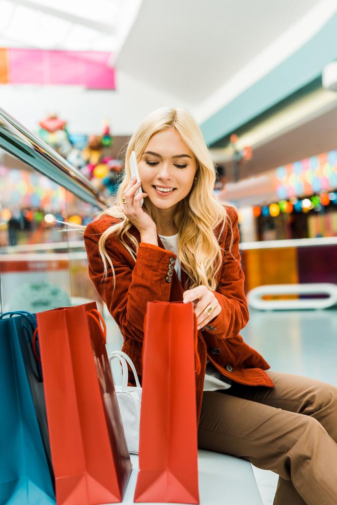 atractiva mujer hablando en el teléfono inteligente y mirando en bolsas de compras
 - Foto, imagen