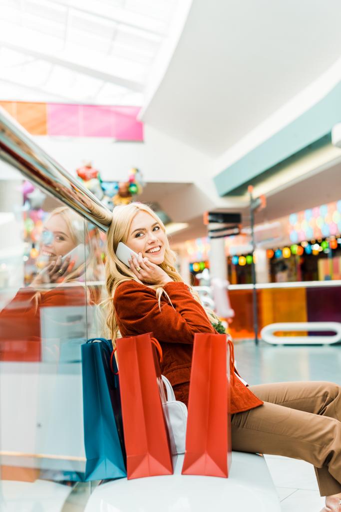 smartphone üzerinde konuşmak ve alışveriş merkezinde alışveriş torbaları ile oturan güzel kız - Fotoğraf, Görsel