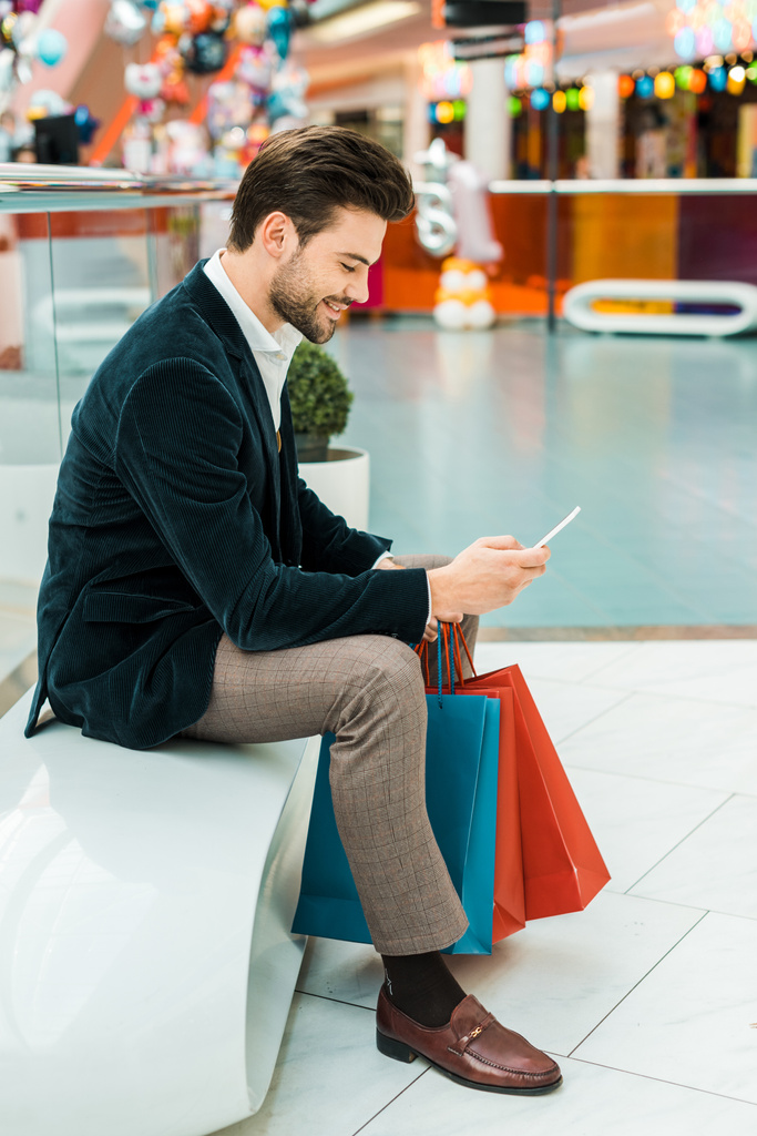 uomo alla moda utilizzando smartphone nel centro commerciale con borse
 - Foto, immagini