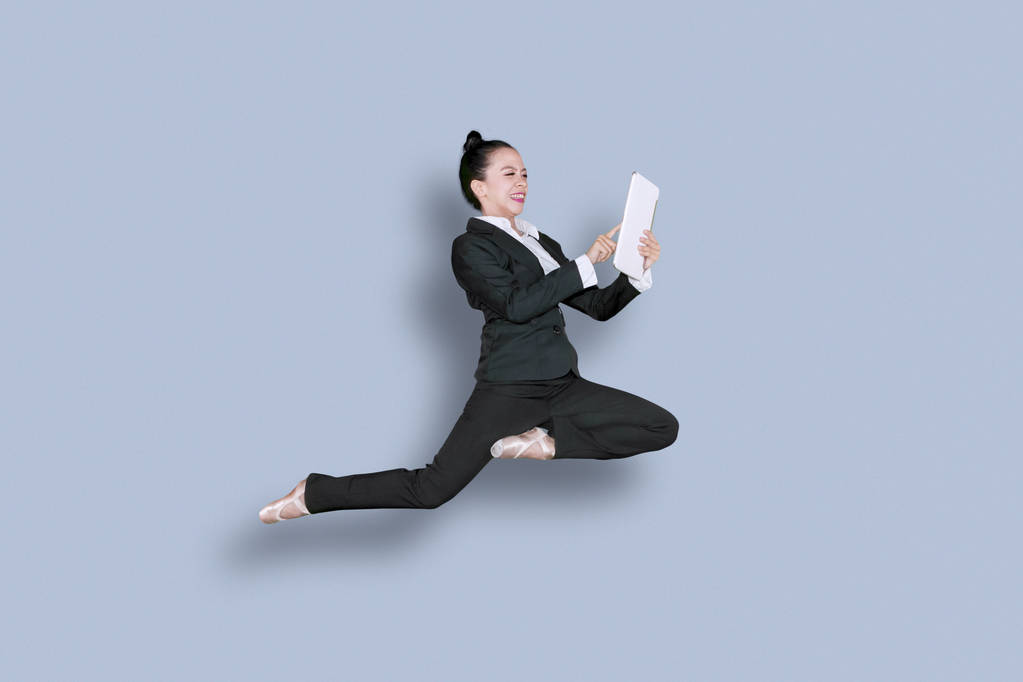 Kuva aasialaisesta liikenaisesta balettikengissä ja tanssimassa studiossa digitaalista tablettia käytettäessä
 - Valokuva, kuva