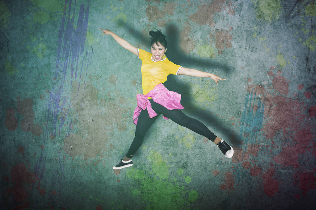 junge Hip-Hop-Tänzerin springt im Studio über einen Wandhintergrund - Foto, Bild