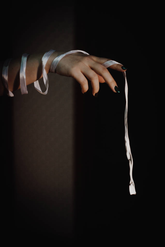 manos atadas con cinta aislada sobre fondo negro resaltado con luz - Foto, imagen