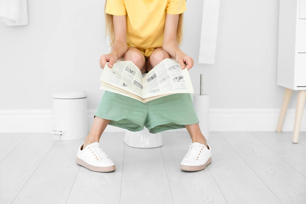 Jonge vrouw krant lezen zittend op de wc-pot thuis - Foto, afbeelding