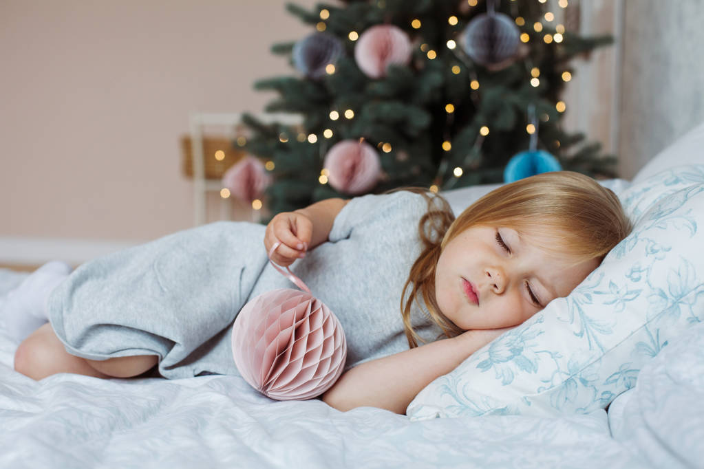 Маленькая девочка спит с игрушкой дома на рождественской елке
 - Фото, изображение