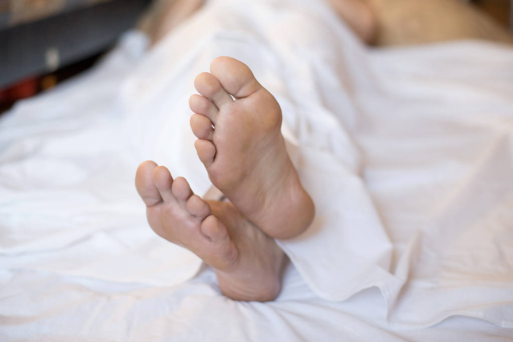 Mies paljain jaloin sängyssä valkoisella pellavalla, valittu painopiste
 - Valokuva, kuva