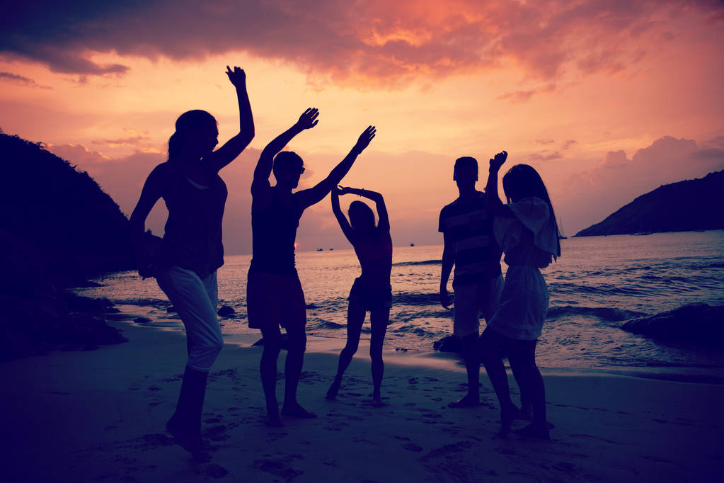 Grupo de personas felices bailando en la playa al atardecer
 - Foto, imagen