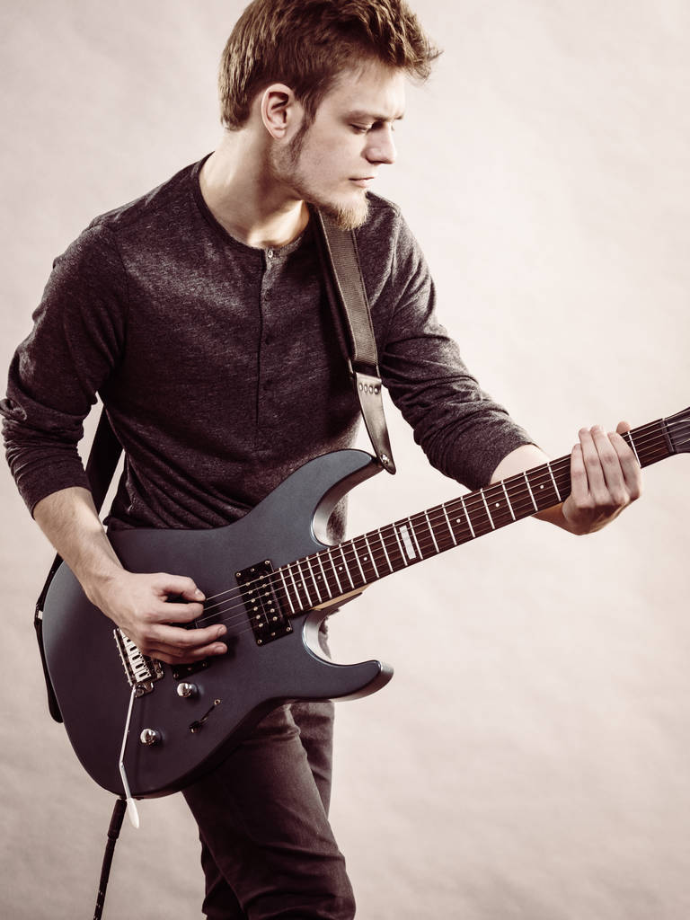Young bearded man with electric guitar. Adult person is holding instrument and playing. Hobby, music concept, on grey - Photo, Image