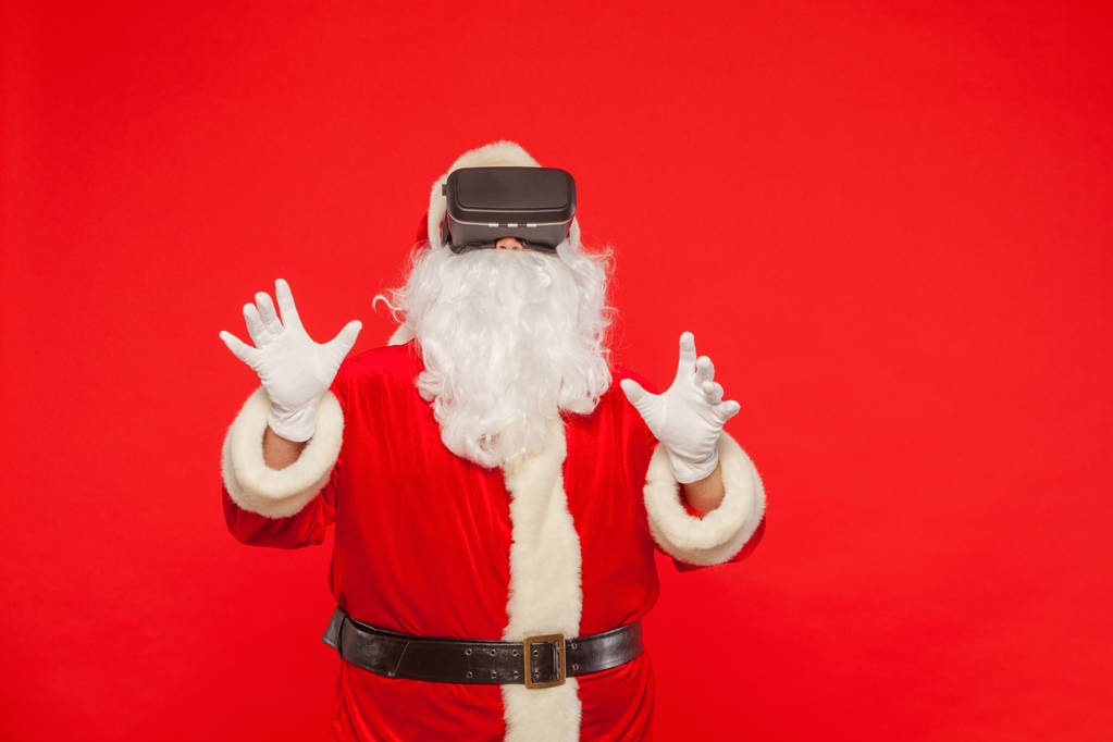 Santa Claus wearing virtual reality goggles, on a red background - Photo, Image