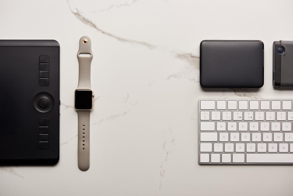 plat lag met grafisch tablet met draagbare hdd, slimme horloge en draadloos toetsenbord op witte marmeren oppervlak - Foto, afbeelding