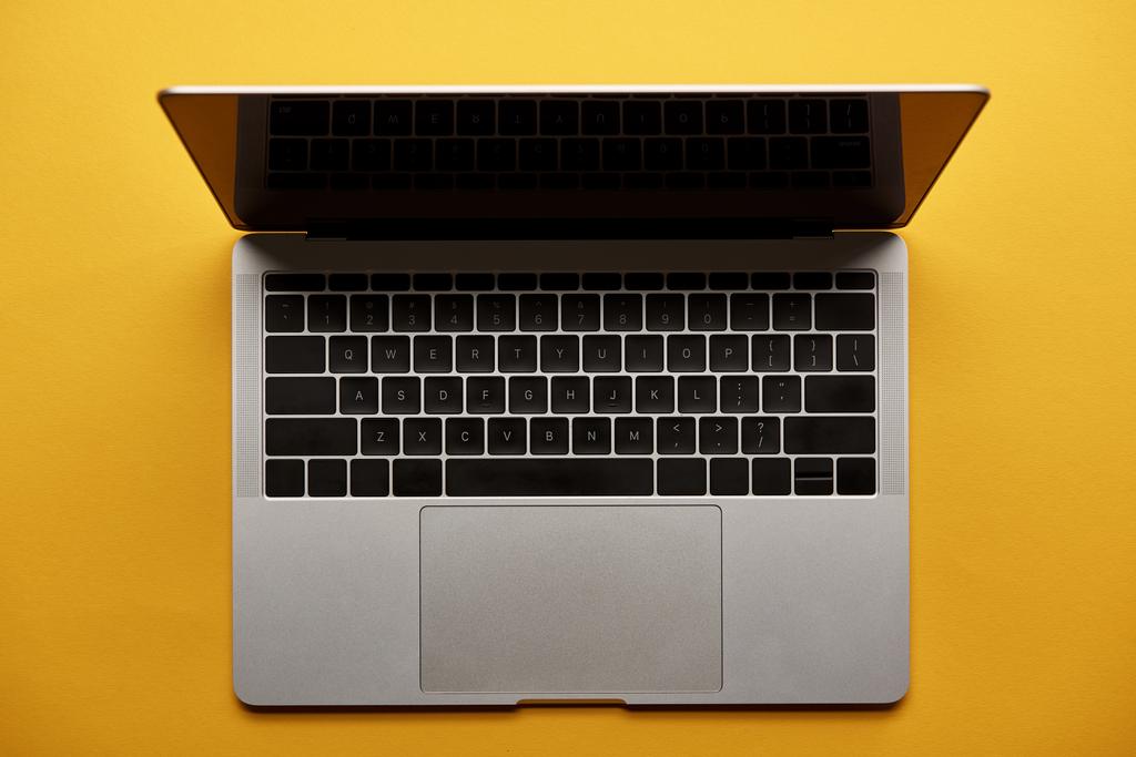 Draufsicht auf geöffneten Laptop auf gelber Oberfläche - Foto, Bild