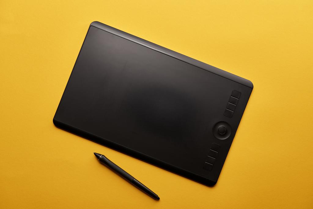 Draufsicht auf Grafik-Tablet und Stift auf gelber Oberfläche - Foto, Bild