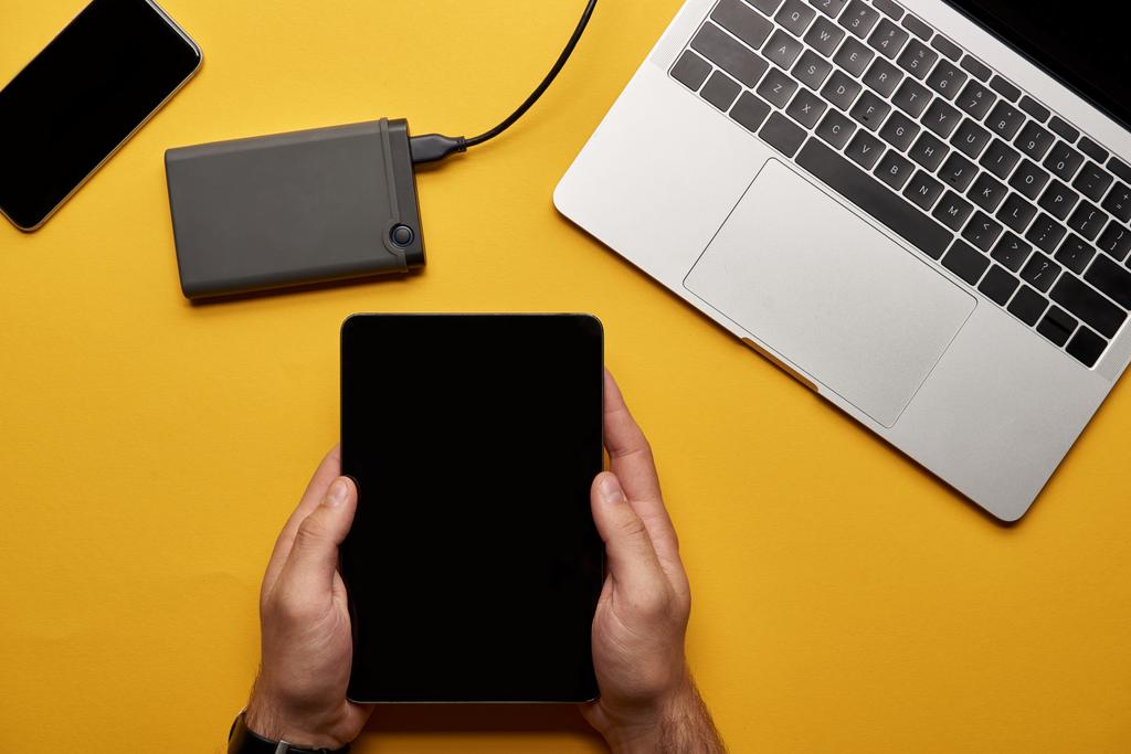 colpo ritagliato di uomo utilizzando tablet su superficie gialla con computer portatile e portatile hdd
 - Foto, immagini