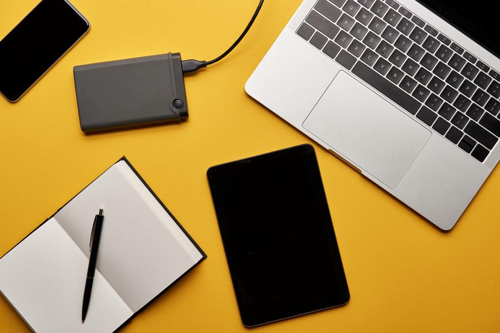 vue de dessus de divers gadgets avec ordinateur portable ouvert couché sur la surface jaune
 - Photo, image
