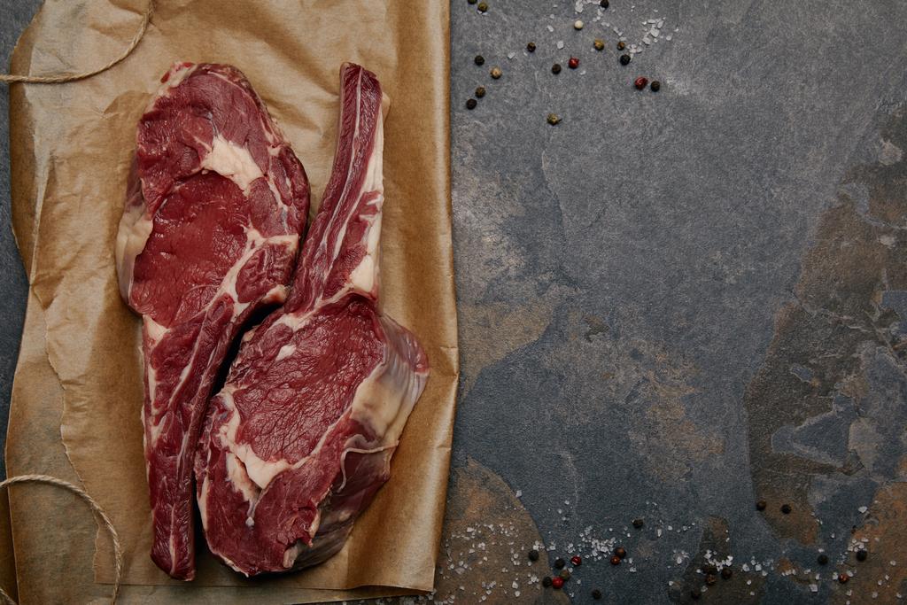 top view of raw rib eye steaks on baking paper with spices on grey background - Photo, Image