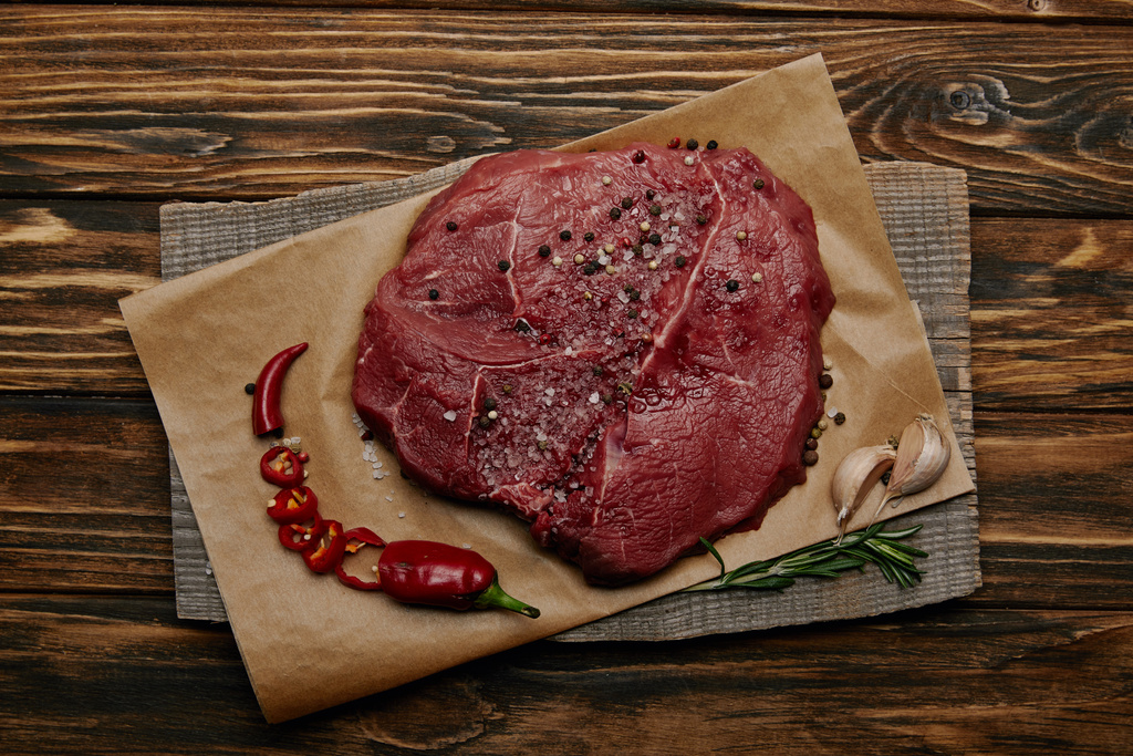 top view of fresh raw meat on baking paper with chopped chilli pepper and garlic on wooden background - Photo, Image