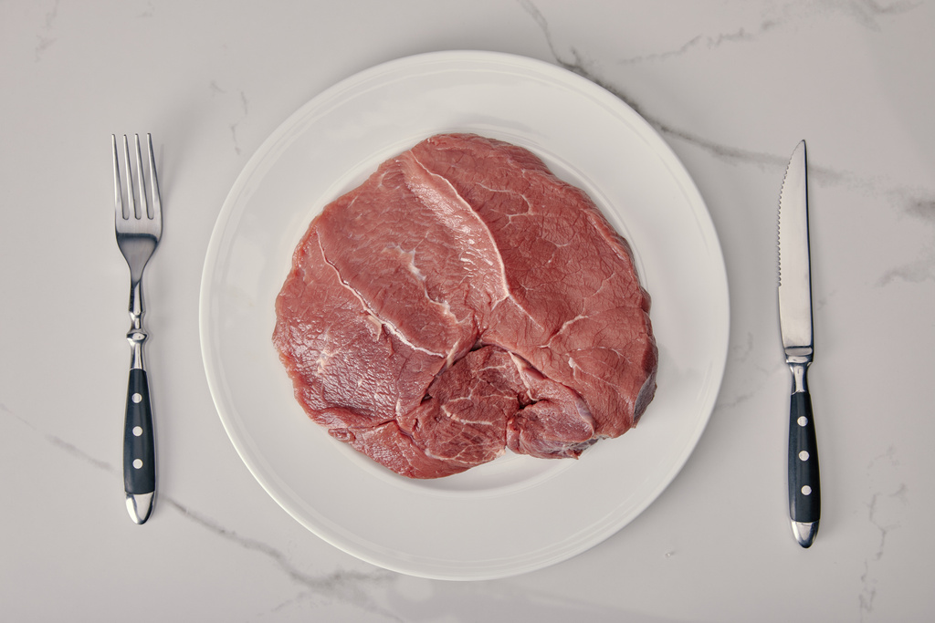 top view of fresh raw meat on plate with kitchen cutlery on white background - Photo, Image