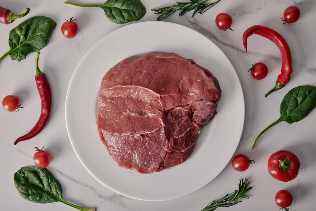 κάτοψη του φρέσκο ωμό κρέας σε πιάτο με λαχανικά και μυρωδικά σε λευκό φόντο - Φωτογραφία, εικόνα
