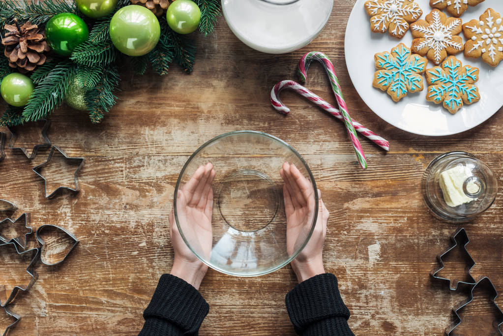 gedeeltelijke weergave van vrouw met lege kom op houten oppervlak met de kroon van Kerstmis en cookies - Foto, afbeelding