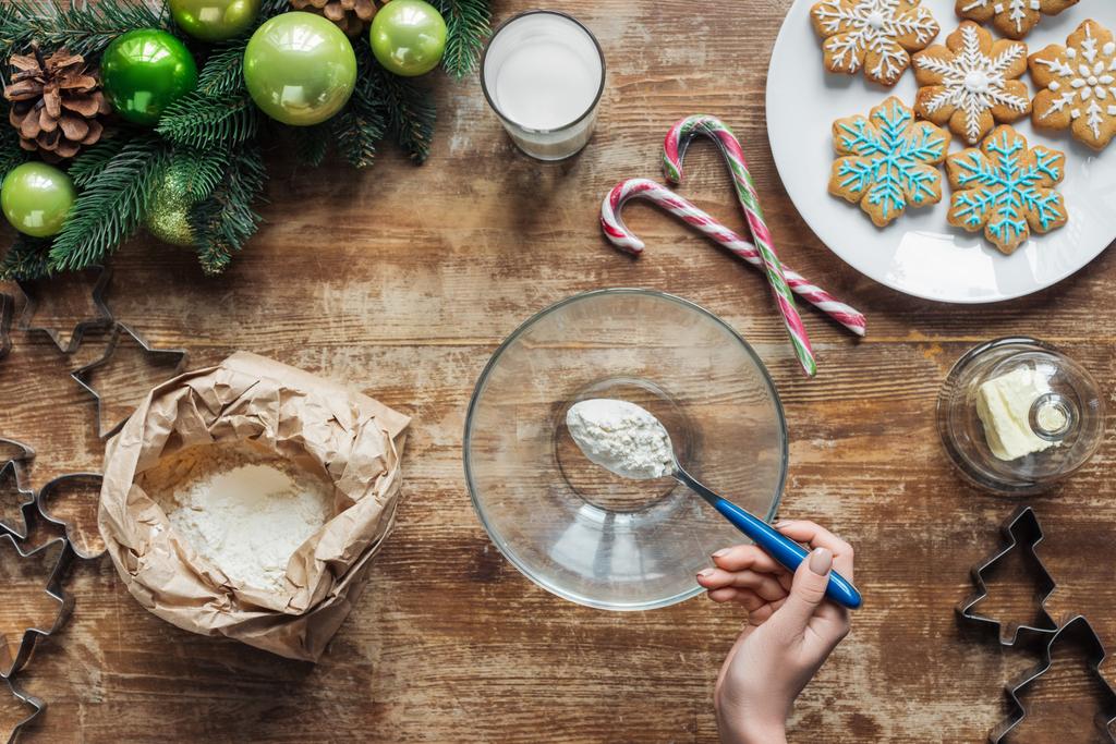 tiro recortado de la mujer verter la harina en el tazón mientras que hace la masa para las galletas de Navidad en la mesa de madera con corona decorativa
 - Foto, imagen