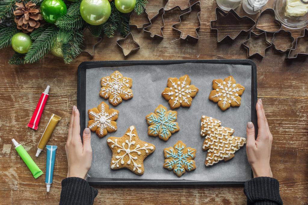 partial view of woman holding baking pan with homemade christmas cookies on wooden surface - Photo, Image