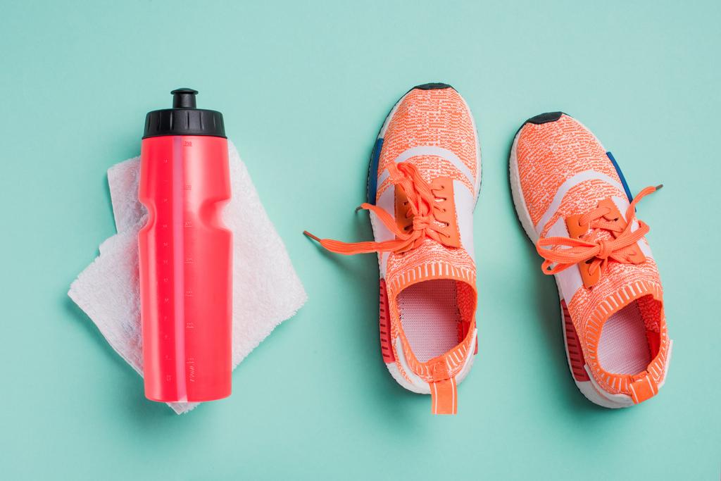 Вид зверху на кросівки, спортивну пляшку та рушник на бірюзовому фоні
 - Фото, зображення