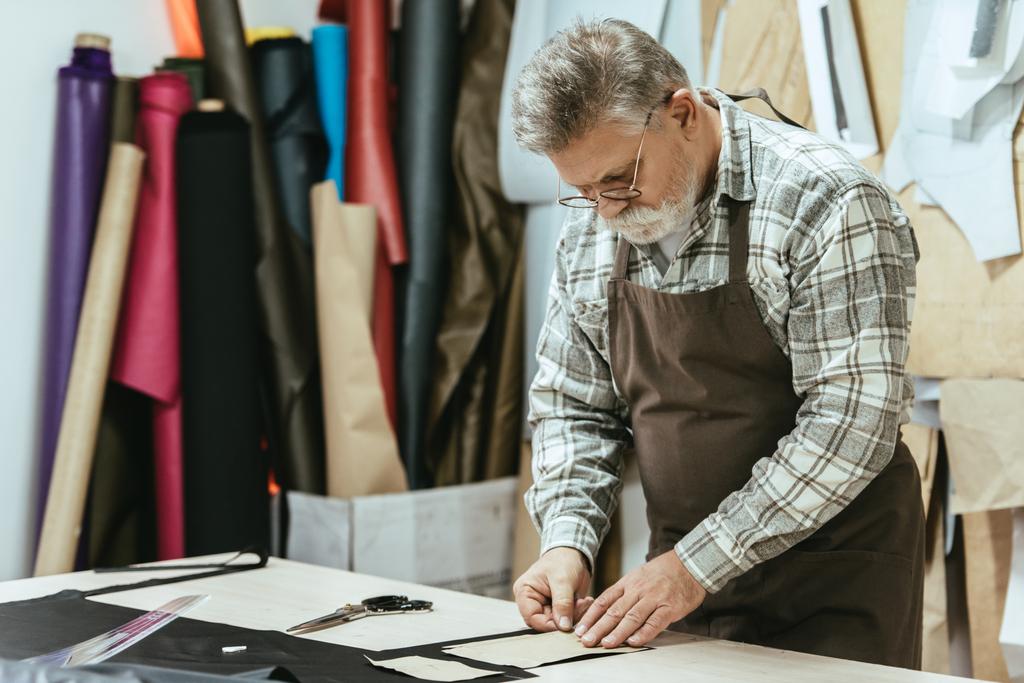 Hombre de mediana edad bolso artesano en delantal y gafas que trabajan en el estudio
 - Foto, imagen