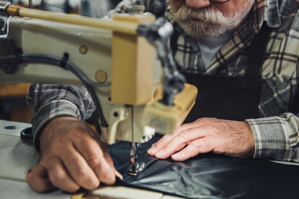 vista parcial del sastre masculino trabajando en la máquina de coser en el estudio
 - Foto, Imagen