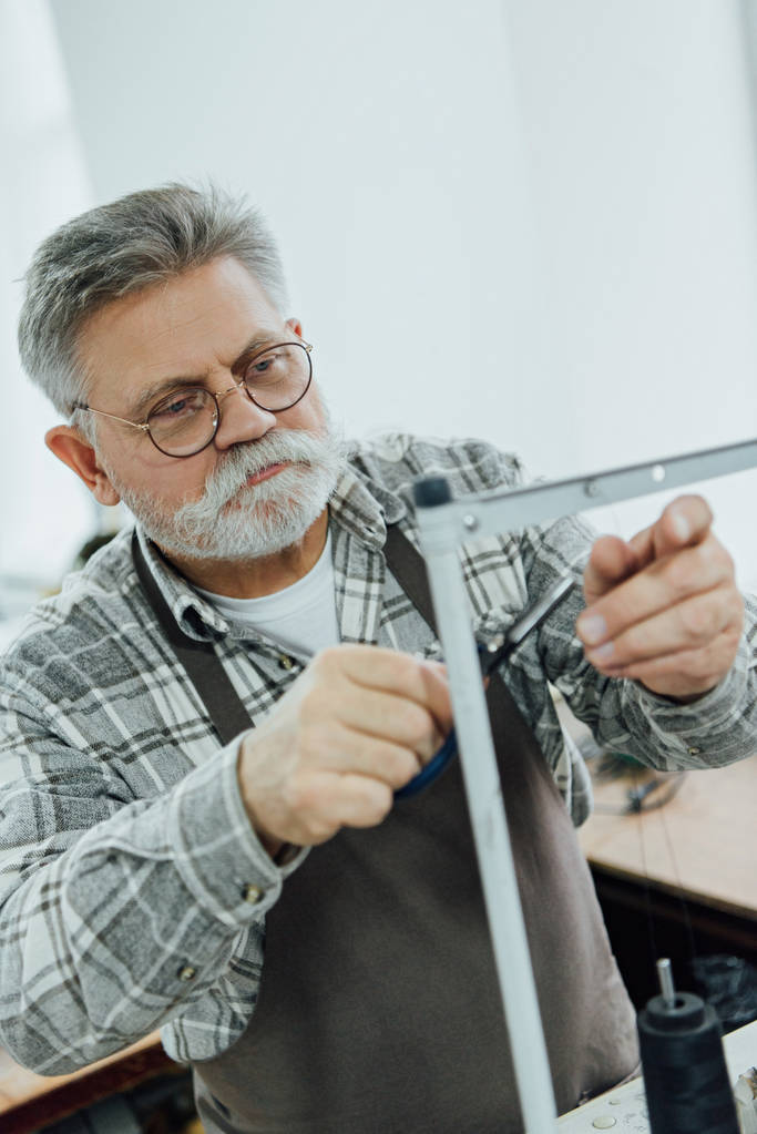 чоловік середнього віку кравець в ріжучих струнах фартуха на швейній машині в майстерні
 - Фото, зображення